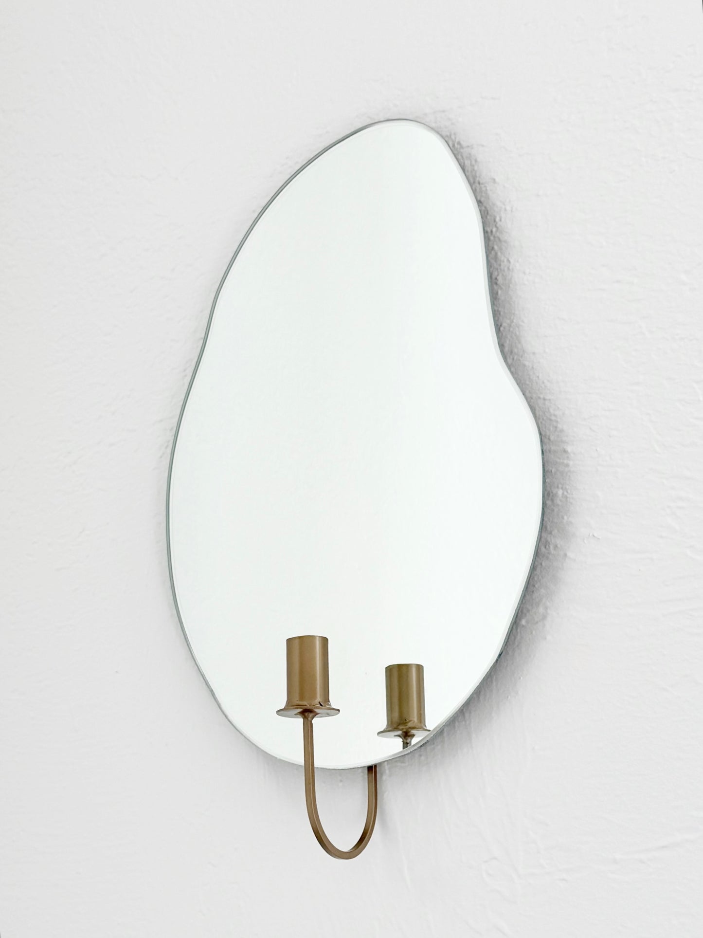 Side angle of the wall mounted organic shape Mar Mirror Candle Sconce or Mirror Candle Holder. The candleholder is gold & not holding a candle. The reflection is of the gold candle holder and white background.