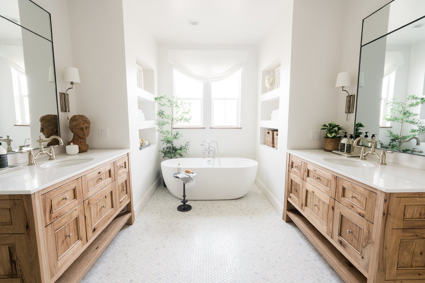 Two custom inlaid mirrors with steel frames facing each other in a large minimalist bathroom with wood and marble vanities and a large freestanding bathtub.