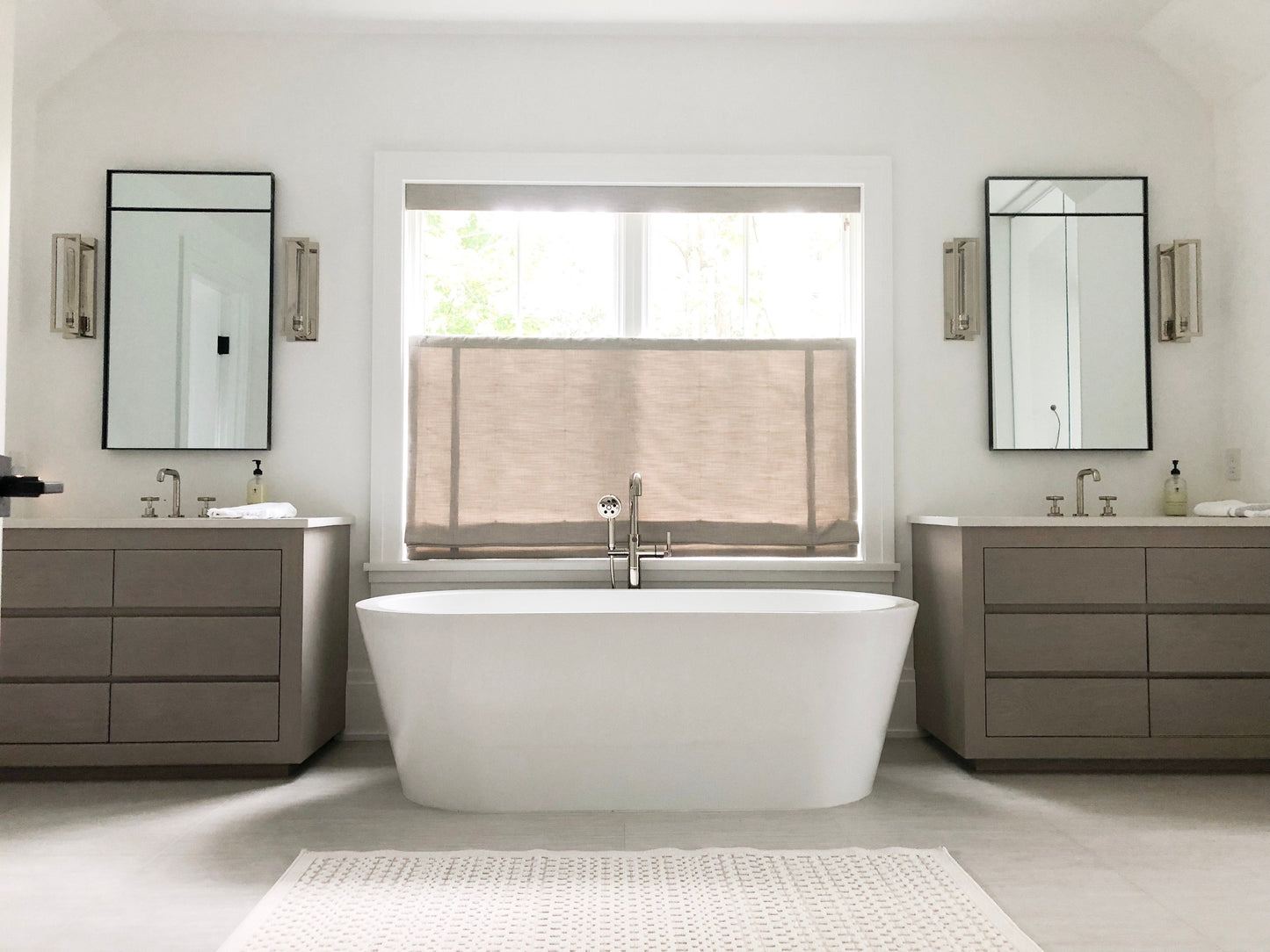 Two custom inlaid steel framed mirrors over two single vanities which are separated by a large white bathtub in a modern bathroom.