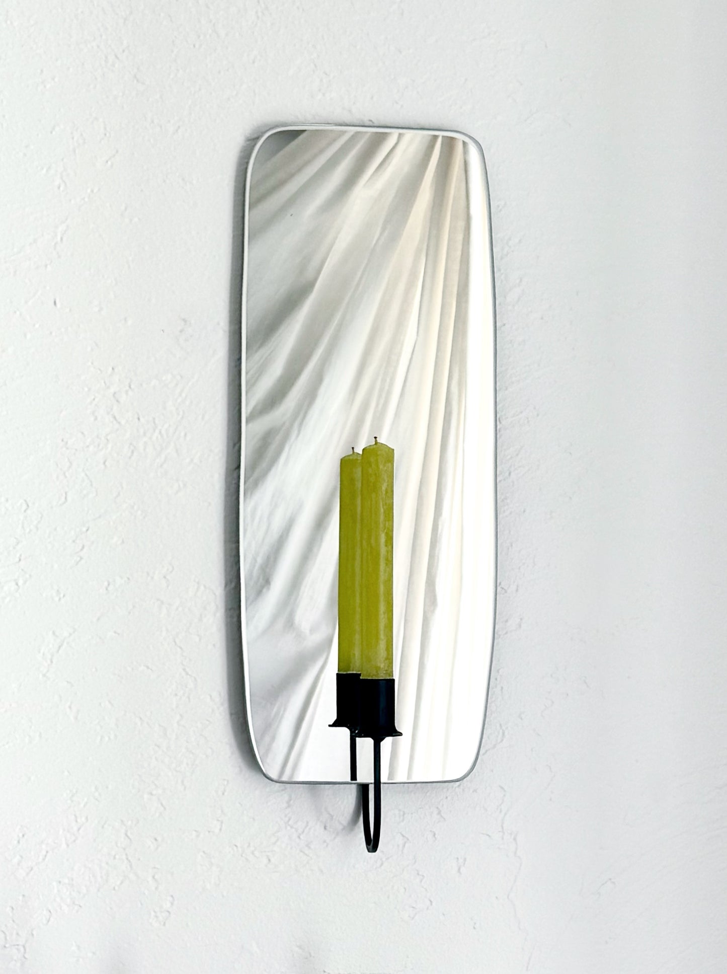 The Oar Mirror Candle Sconce or Mirror Candle Holder, wall mounted, reflecting the black candleholder holding a green unlit candle and a cream backdrop.