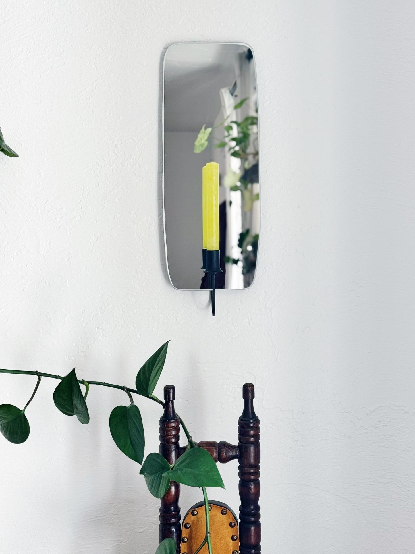 Mirror Candle Sconce or Mirror Candle Holder wall mounted. The black candleholder has a green unlit candle. Reflection is of the candle holder, candle, plants & cozy room decor.