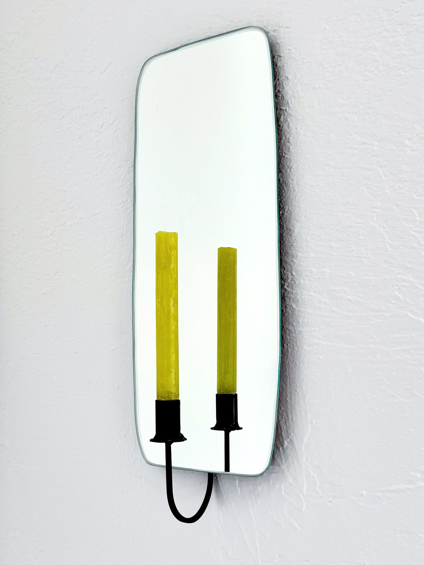 Side view of the Oar Mirror Candle Sconce or Mirror Candle Holder, wall mounted, reflecting the black candleholder holding a green unlit candle and a white backdrop.