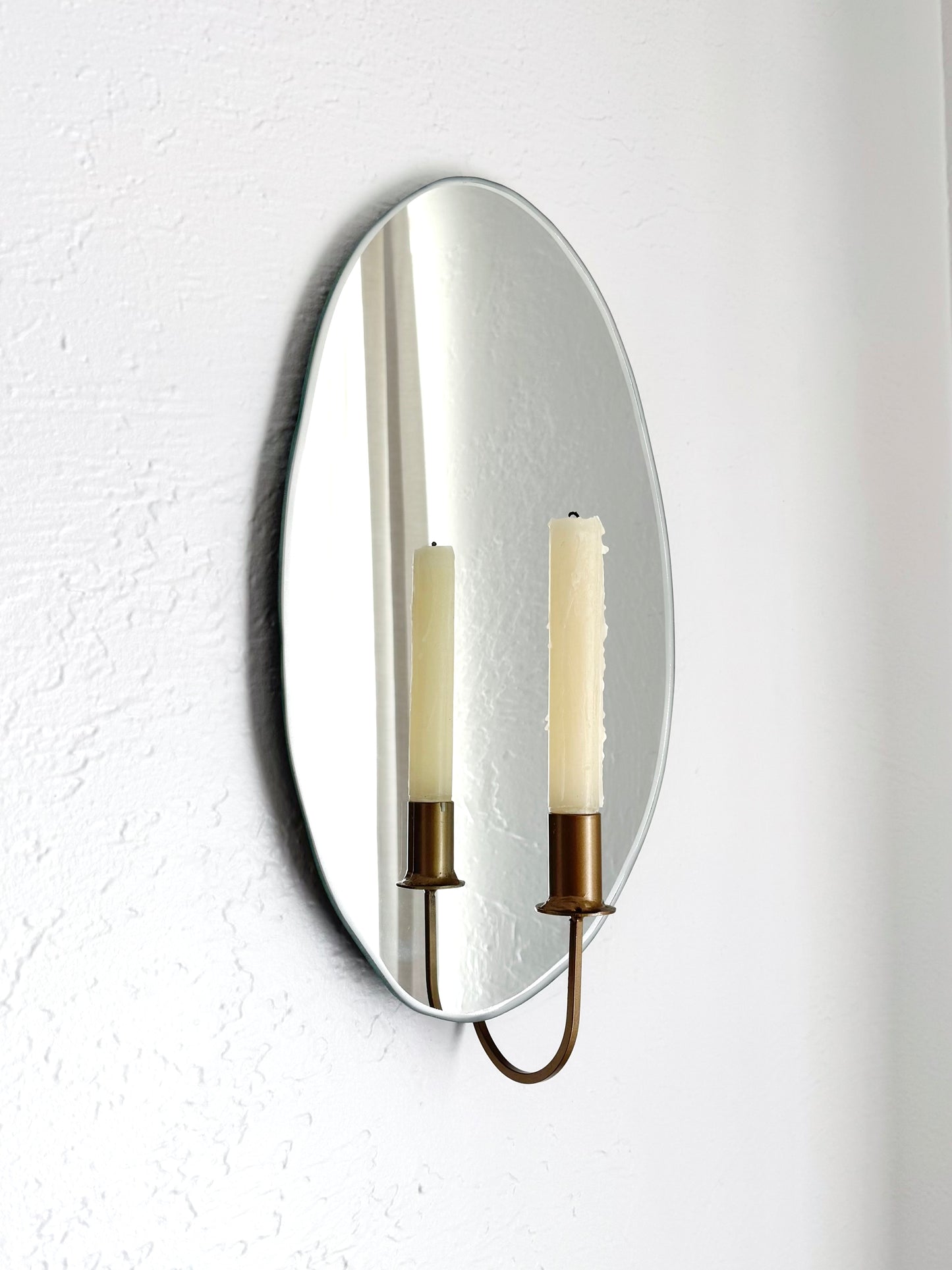 Side view of the Mirror Candle Sconce or Mirror Candle Holder, wall mounted, with gold candleholder and a cream unlit candle. The reflection shows the gold candle holder, candle, & light backdrop.