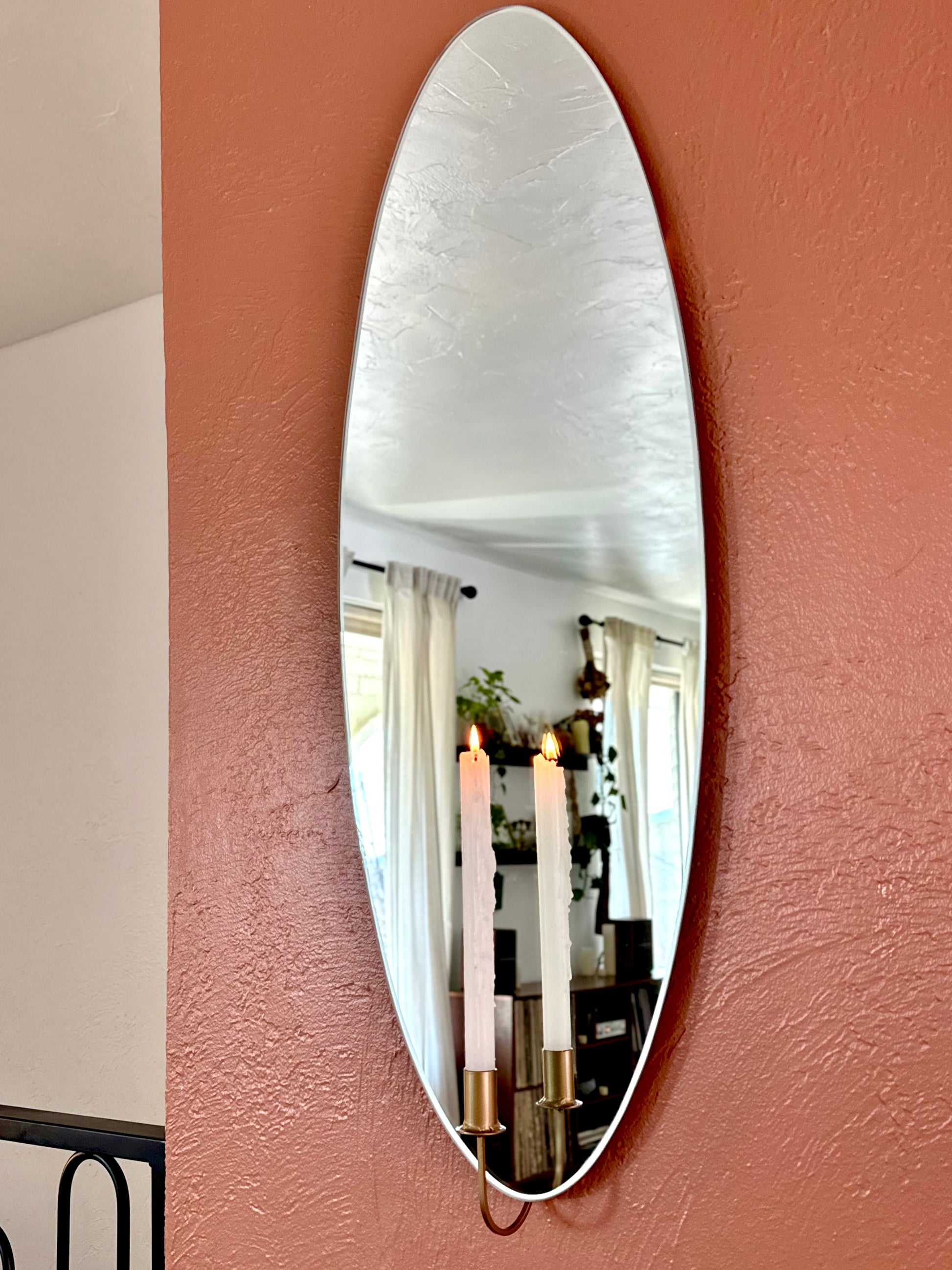 Medium/Large wall mounted frameless mirror candle sconce or mirror candle holder on a terracotta painted wall. The gold candleholder is holding a white lit candle. The reflection is of the candle & candle flame glowing giving cozy home vibes.